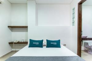 a bedroom with a white bed with two blue pillows at Hotel Ayenda Boutique Rio Mont in Montería