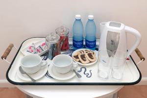 a tray with a tea kettle and cups and water bottles at Boulders Beach Hotel, Cafe and Curio shop in Simonʼs Town