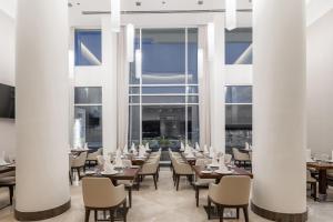 un restaurante con columnas blancas, mesas y sillas en Qamar Hotel Jeddah en Yeda
