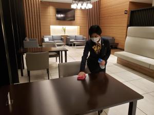 Una mujer con una máscara parada en una mesa en Smile Hotel Towada, en Towada