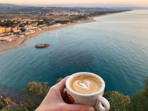 a hand holding a cup of coffee overlooking a beach at Luna Convento Copanello B&B in Stalettì