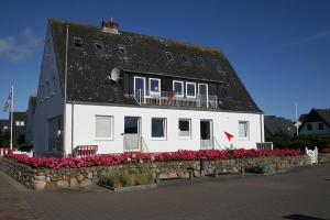 a large white building with a black roof and flowers at Am Wasser 4 OG in Hörnum