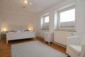 ein weißes Schlafzimmer mit einem Bett und zwei Fenstern in der Unterkunft Ferienhaus TerpMeren in Hörnum
