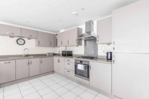 a kitchen with white cabinets and a clock on the wall at 2 BED & 2 BATH COSY APARTMENT SLOUGH- FREE PARKING in Slough
