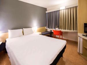 um quarto de hotel com uma grande cama branca e uma cadeira vermelha em ibis Araçatuba em Araçatuba