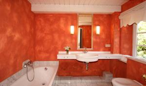 uma casa de banho com paredes vermelhas, um lavatório e uma banheira em Ferienhäuser im Sylter Gartenweg em Tinnum