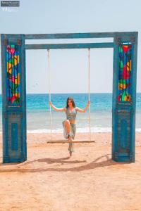 a woman sitting on a swing on the beach at Ecotel Dahab Bay View Resort in Dahab