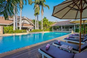 a swimming pool with lounge chairs and an umbrella at Le Charme Sukhothai Historical Park - SHA Extra Plus in Sukhothai