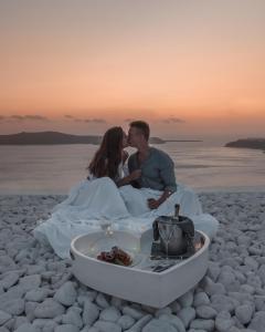 a bride and groom sitting on the beach kissing at Cavo Tagoo Santorini in Imerovigli