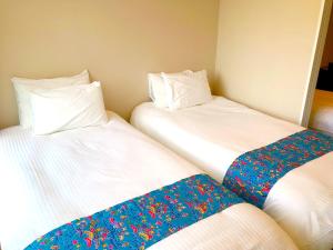 Dos camas en una habitación con sábanas blancas con flores. en Tenpoint Hotel OKOU en Naha