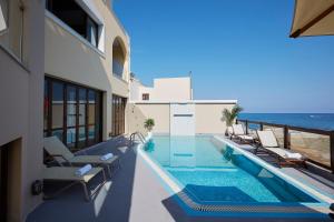 a swimming pool with chairs and the ocean in the background at Villa Andreas in Panormos Rethymno