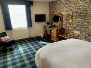 a bedroom with a bed and a desk and a television at Hal O' The Wynd Guest House in Stornoway