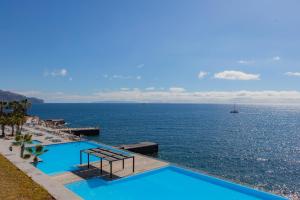 
a beach with a pool and chairs and a blue sky at VidaMar Resort Hotel Madeira - Dine Around Half Board in Funchal

