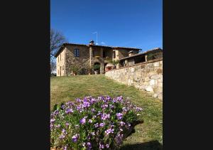 una casa de piedra con flores púrpuras delante de ella en Casalgallo en Quercegrossa