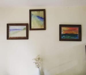 three paintings on a white wall with a vase at Tropical land little Hanoi homestay in Hanoi
