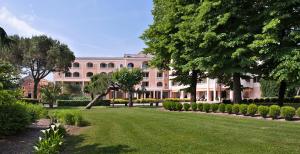 een groot roze gebouw met bomen en een gazon bij Hotel Terme Neroniane in Montegrotto Terme