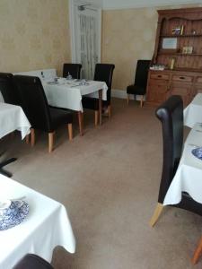 uma sala de jantar com mesas brancas e cadeiras pretas em Moorfield Hotel em Llandudno