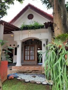 una piccola casa bianca con un albero di fronte di OMAH LUMUT Malang, Best Family Villa 3 Bedrooms Free Pool Kolam Renang a Malang