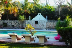 a swimming pool with benches next to a stone wall at Hotel Puerta Chichen in Chichén-Itzá