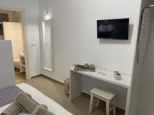 a white bedroom with a desk and a tv on the wall at Levanda Guest Houses in Andiparos
