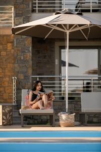 a woman sitting in a chair under an umbrella at Costa D' Ifesto in Agios Ioannis Kaspaka
