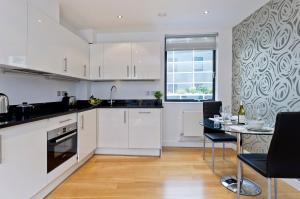 uma cozinha com armários brancos e uma mesa com cadeiras em Red Lion Court by City2Stay em Londres