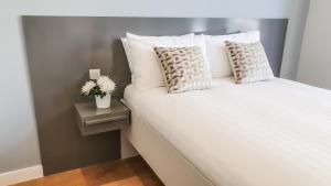 un letto con lenzuola e cuscini bianchi di Cromwell Serviced Apartments by StayPrime a Londra