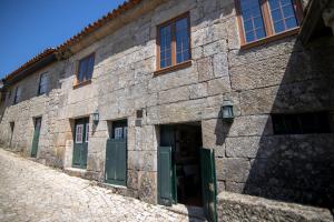 a stone building with green doors on a street at Casa do Campanário in Sortelha