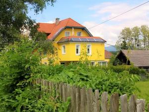 ein gelbes Haus mit rotem Dach hinter einem Zaun in der Unterkunft Kunterbunt Seehaus in Faak am See