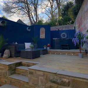 eine Terrasse mit einer Bank und einer blauen Wand in der Unterkunft Rose Cottage in Morpeth