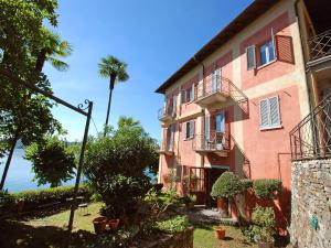 a pink building with a palm tree next to the ocean at Studio Casa sul lago by Interhome in Orta San Giulio