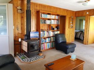 a living room with a stove and a chair and book shelves at Awesome View Cottage in Great Barrier Island