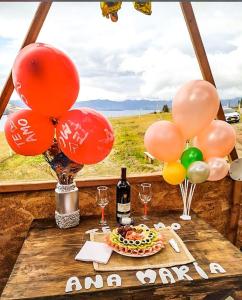 una mesa con globos y un pastel y una botella de vino en GLAMPING Aldea Muisca, en Tota