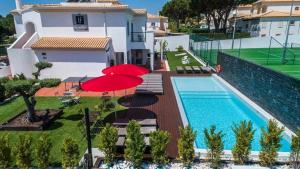 a house with a swimming pool and two red umbrellas at Villa w Private Pool Tennis Courts e Golf Putt in Vilamoura