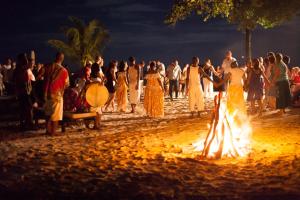 een groep mensen die rond een kampvuur op het strand staan bij Paradise Sun Hotel Seychelles in Baie Sainte Anne