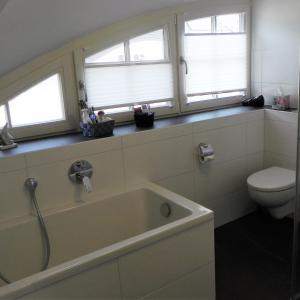 ein Badezimmer mit einer Badewanne und einem WC sowie zwei Fenster in der Unterkunft Dünenperle in Zingst
