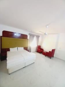 a bedroom with a white bed and two red chairs at Discovery Duqm Apartment in Duqm