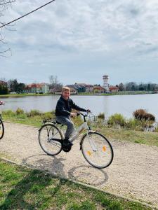 un hombre montando una bicicleta en un camino junto a un lago en Happy Mammy Bababarát Apartmanház 1 - Hűvös utca, en Orosháza