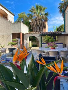 un patio avec des tables et des fleurs devant un bâtiment dans l'établissement Logis Hôtel Les II Mas - Perpignan Sud, à Cabestany