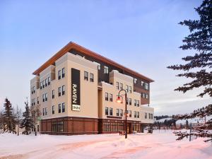 Un gran edificio en la nieve con árboles al frente. en Raven Inn Whitehorse, en Whitehorse