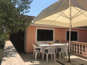 a table with chairs and an umbrella in front of a house at Apartmani Vilma Pakoštane in Pakoštane