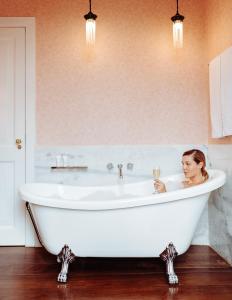 a woman sitting in a bath tub with a glass of wine at Hotel Reggia Catarina in Petrópolis