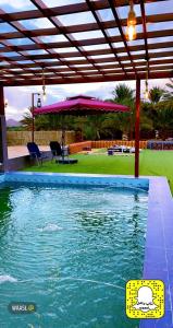 una piscina con sombrilla, mesa y sillas en أستراحة مون لايت الريفي en Al Ula