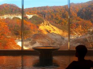 a person standing in front of a window looking at a mountain at Dai-ichi Takimotokan in Noboribetsu