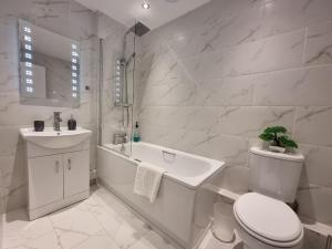 a white bathroom with a toilet and a tub and a sink at 144 - ExcellentStays - 2 Bedroom Flat in Stanwell