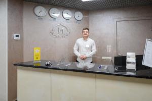 un hombre parado detrás de un mostrador en una habitación con relojes en Ilinka Hotel en Vladimir