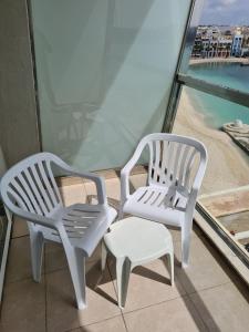 two white chairs and a stool on a balcony at Water's Edge Hotel in Birżebbuġa