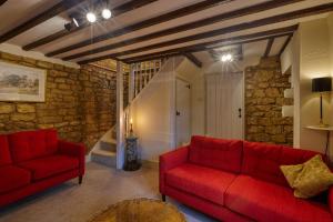 Fab 2 Bed Cotswolds Cottage with Private Courtyard : غرفة معيشة بها أرائك حمراء وجدار حجري