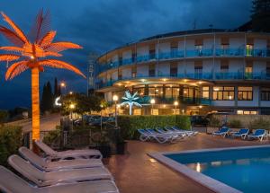 a hotel with chairs and a palm tree and a pool at Hotel Caribe - Garda Lake Collection in Brenzone sul Garda