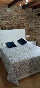 a bed with blue pillows in a room with a stone wall at Apartamentos Fons sacrata in Fonsagrada